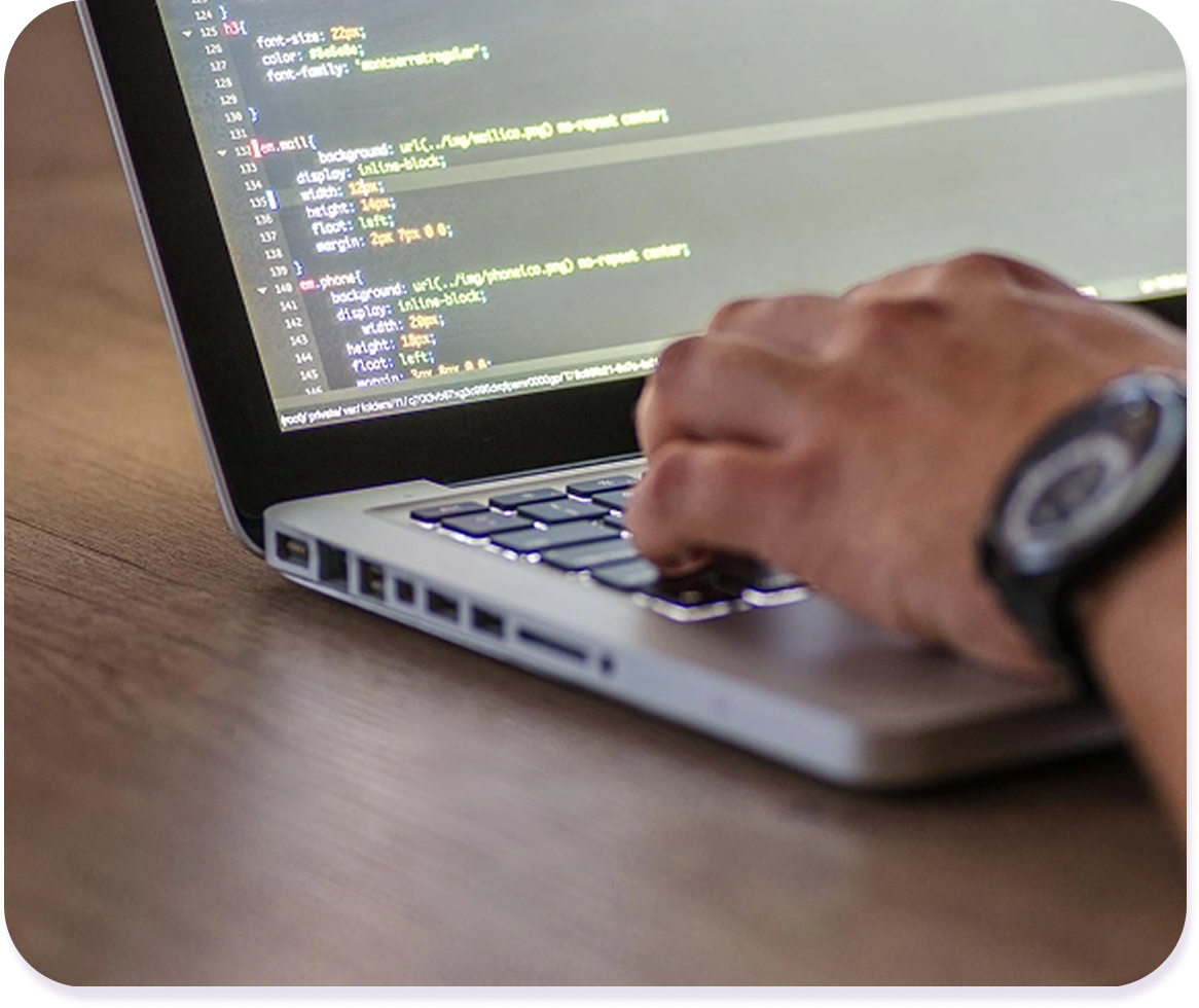 Detalle mano tecleando en un ordenador con líneas de código en la pantalla